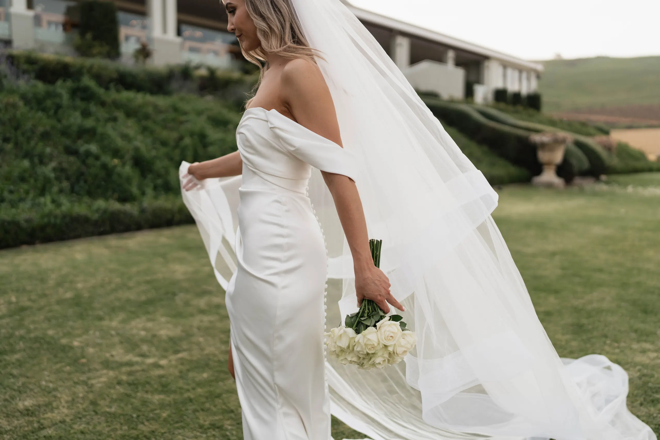 Bride on the lawn holding her bouquet and flowing veil