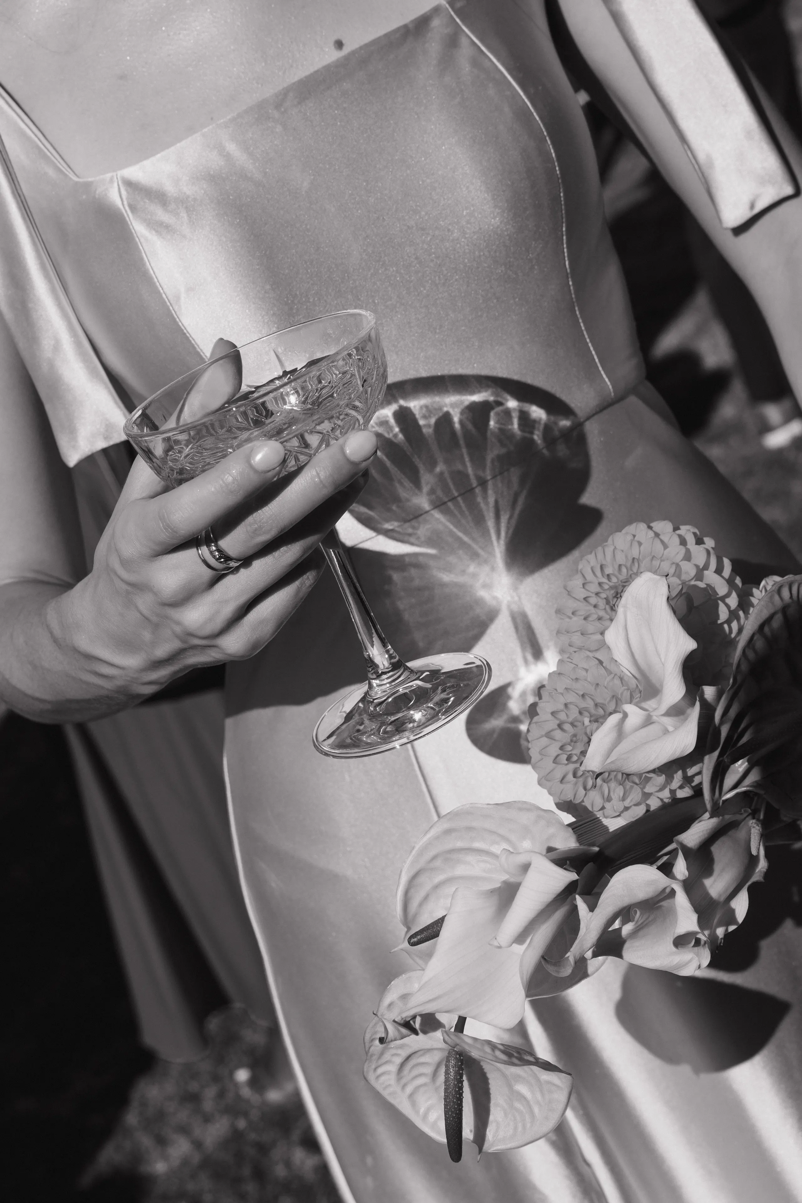 Black-and-white detail of a hand holding a cocktail beside wedding flowers