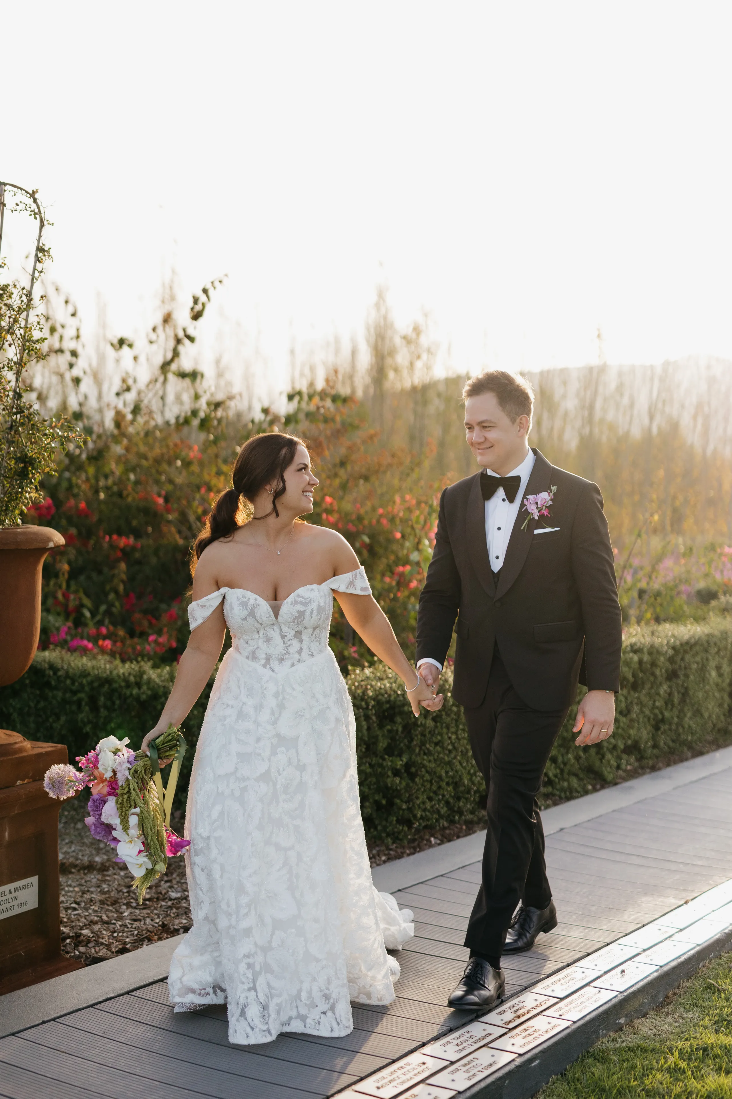 Bride and groom walking hand in hand through a flower garden in golden evening light