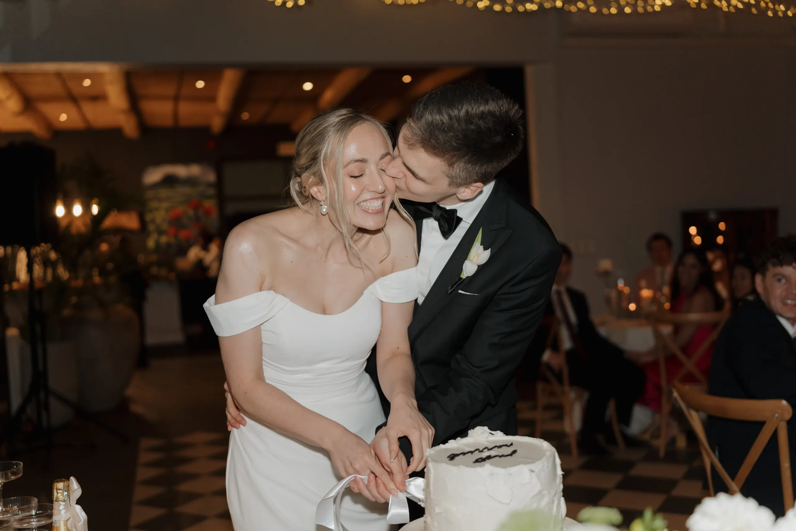 Groom kissing the bride's cheek as they cut their wedding cake