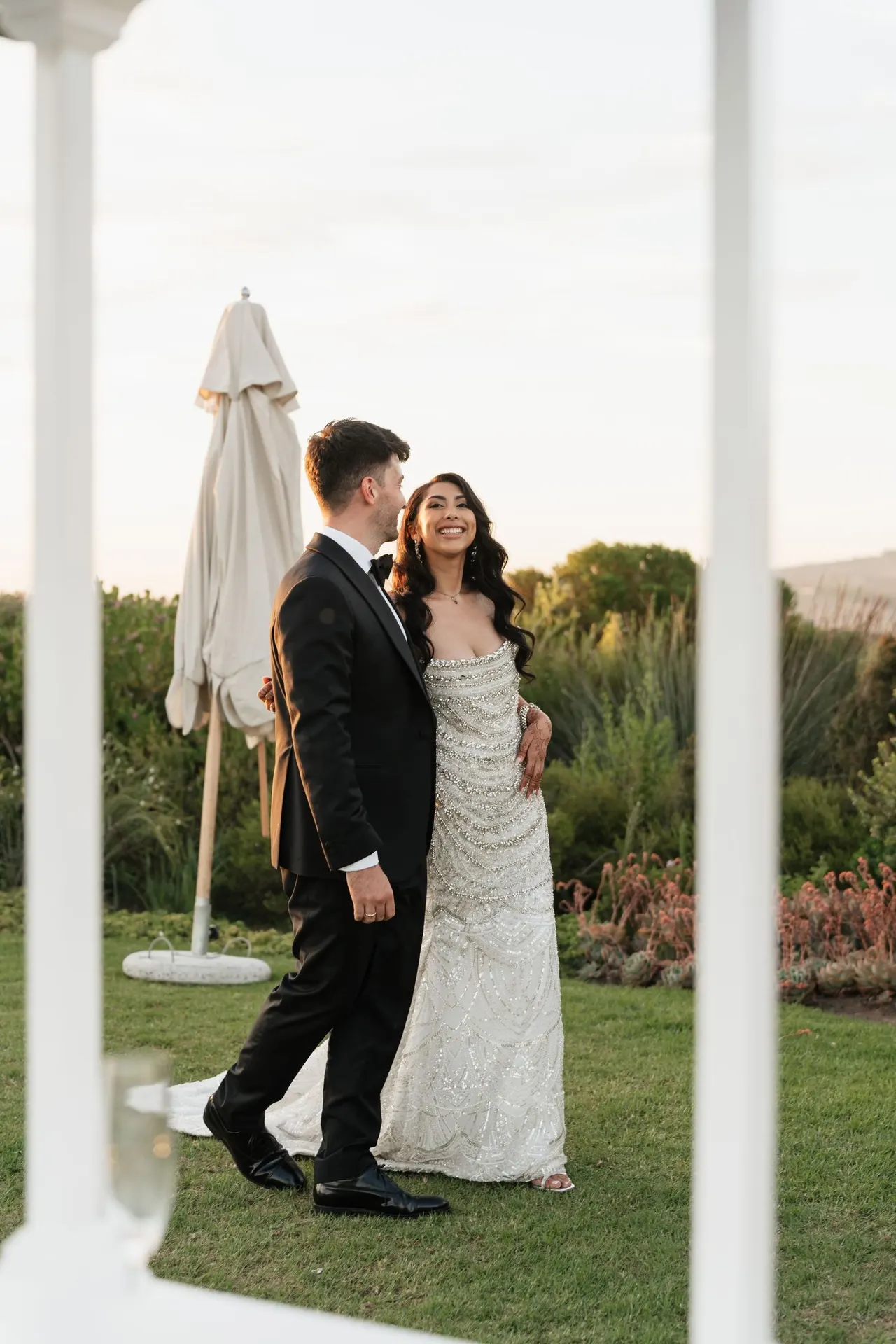 Groom kissing the bride beside a garden parasol at golden hour