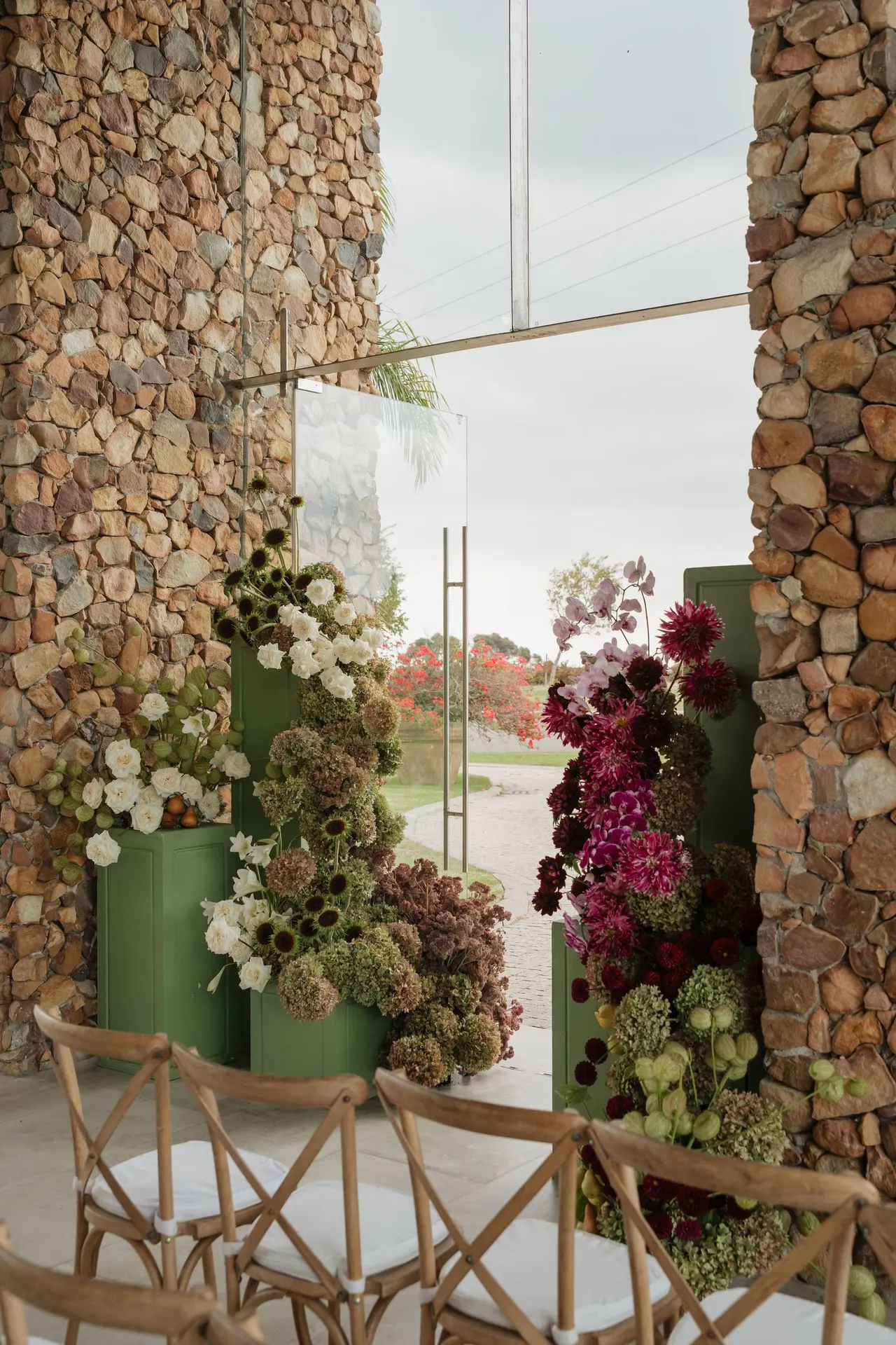 Floral installation in pinks and reds against a stone wall entrance