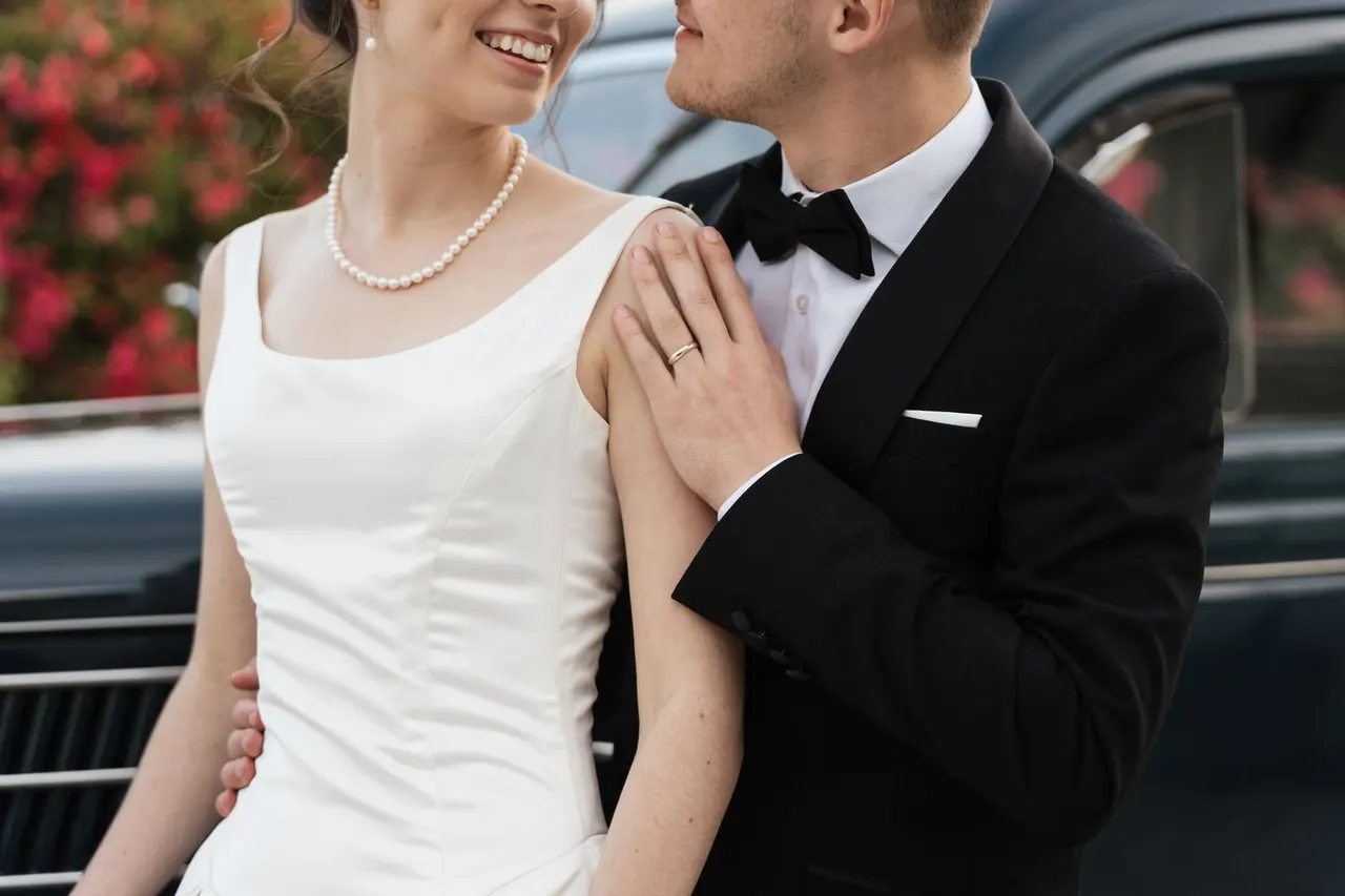 Close detail of the couple — pearls, satin and a black tuxedo
