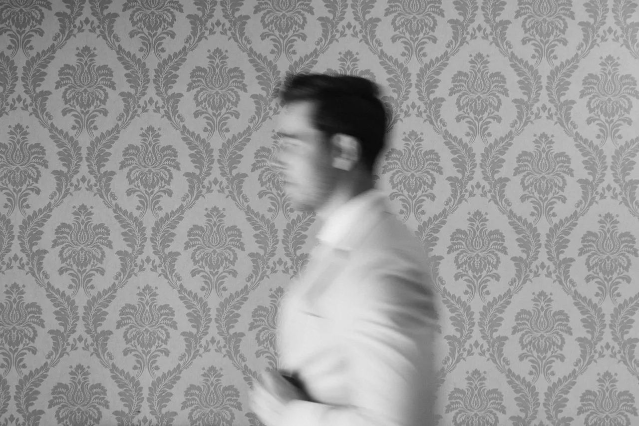 Black-and-white motion blur of the groom against damask wallpaper