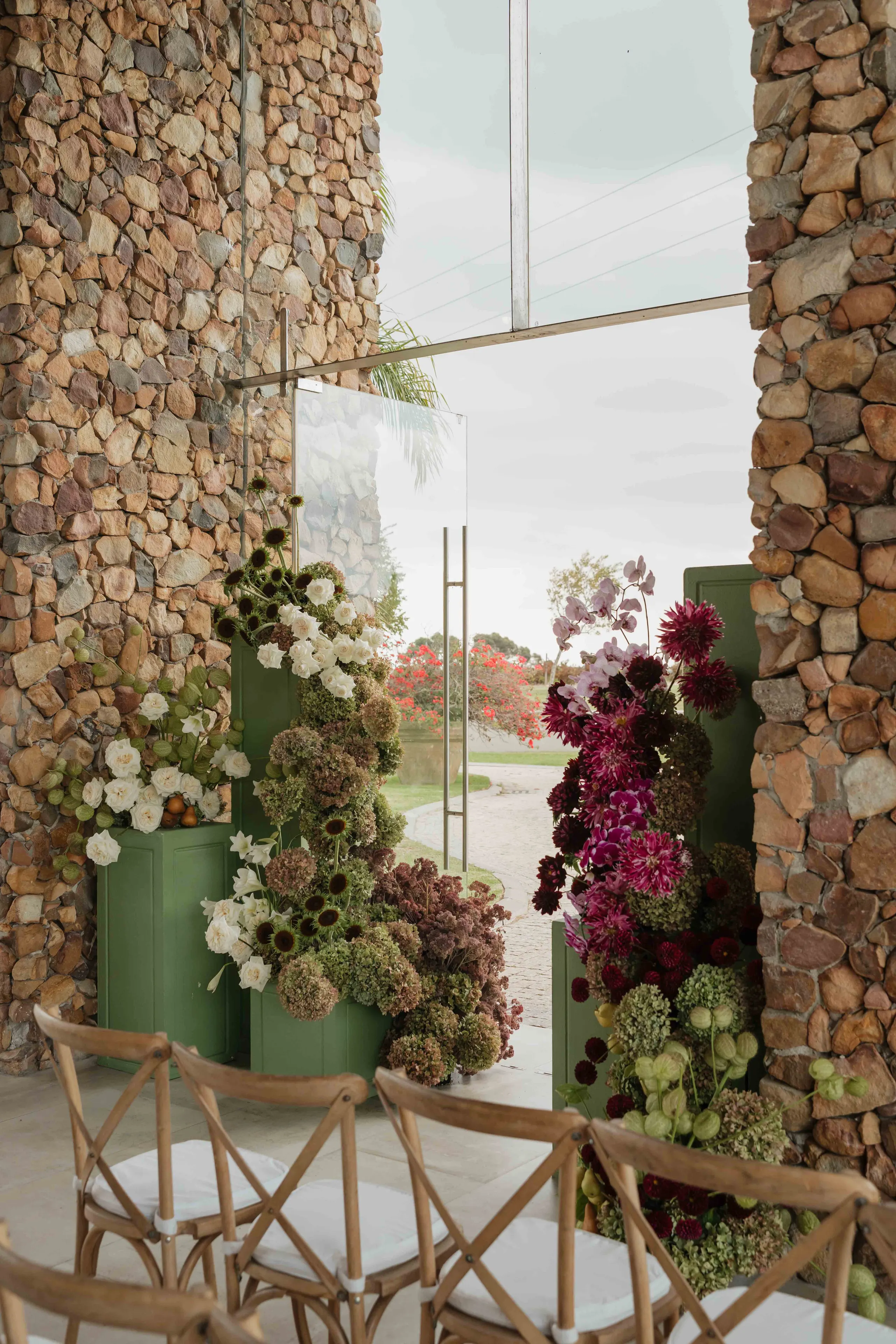 Ceremony floral installation in deep reds and whites against a stone wall