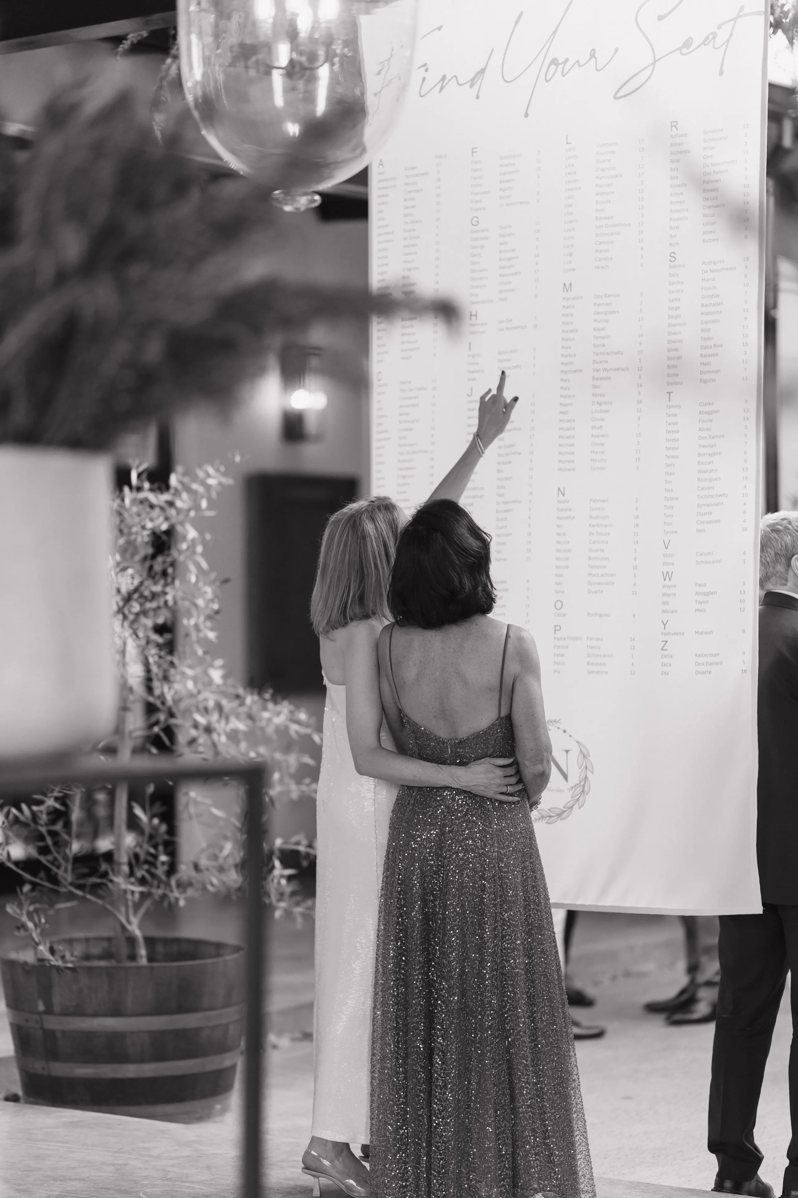 Black-and-white moment of guests finding their names on the seating chart under fairy lights