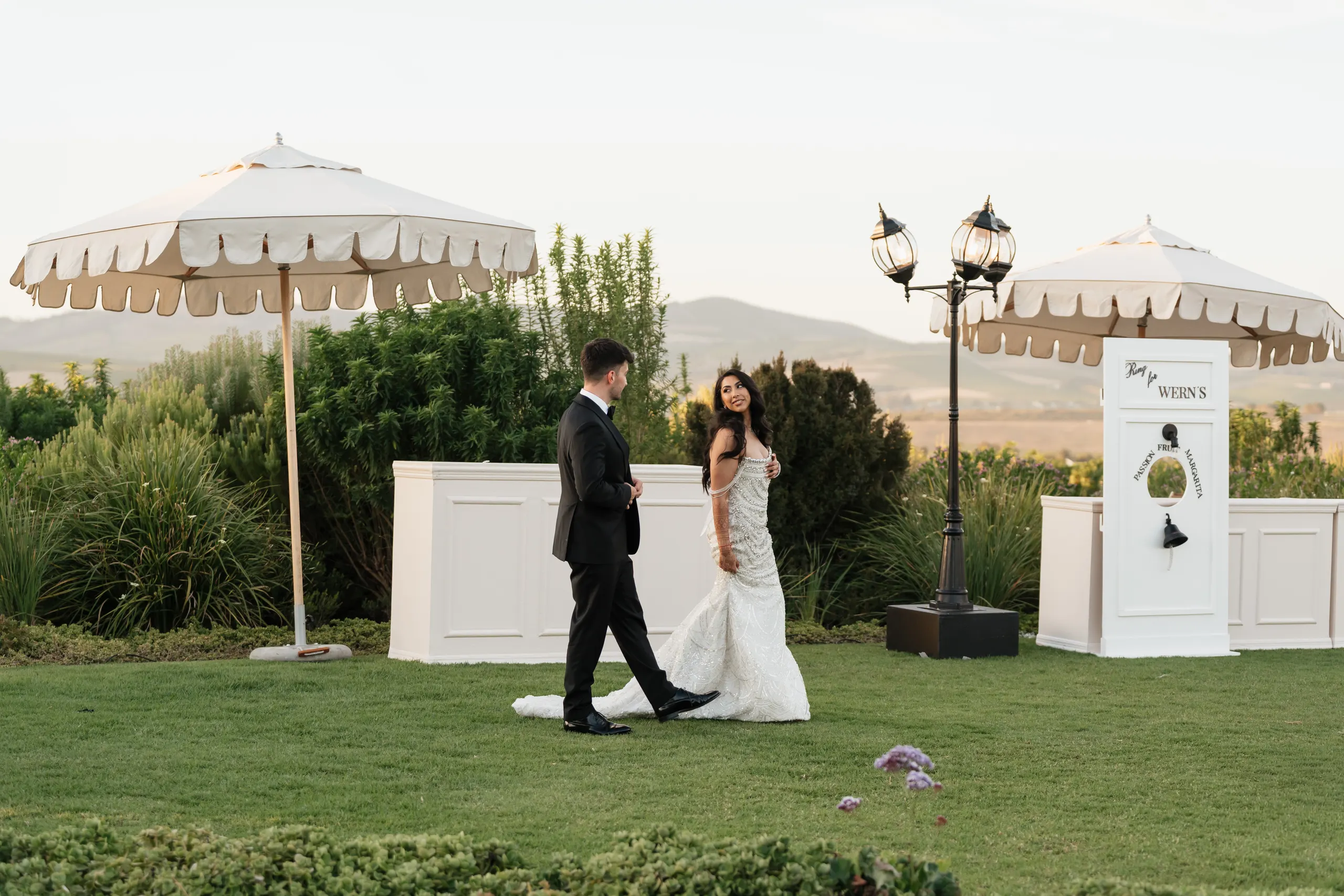 Garden ceremony setting with ornate lamp posts and a parasol at golden hour